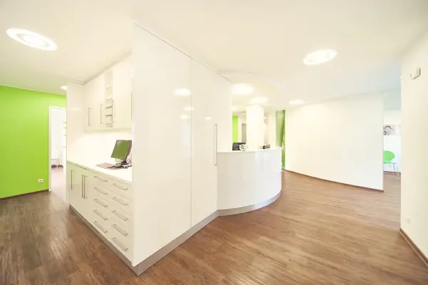 Moderne Arztpraxis mit Empfangstresen, grünen Wänden und heller, freundlicher Einrichtung.