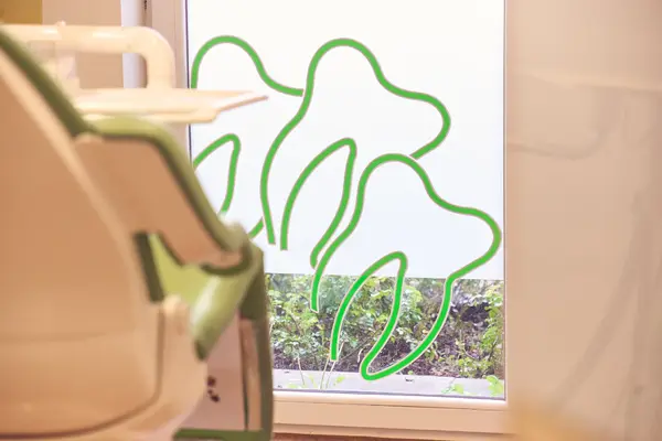 Zahnarztpraxis mit grünem Zahnmotiv auf Fensterscheibe und Behandlungsstuhl im Vordergrund.
